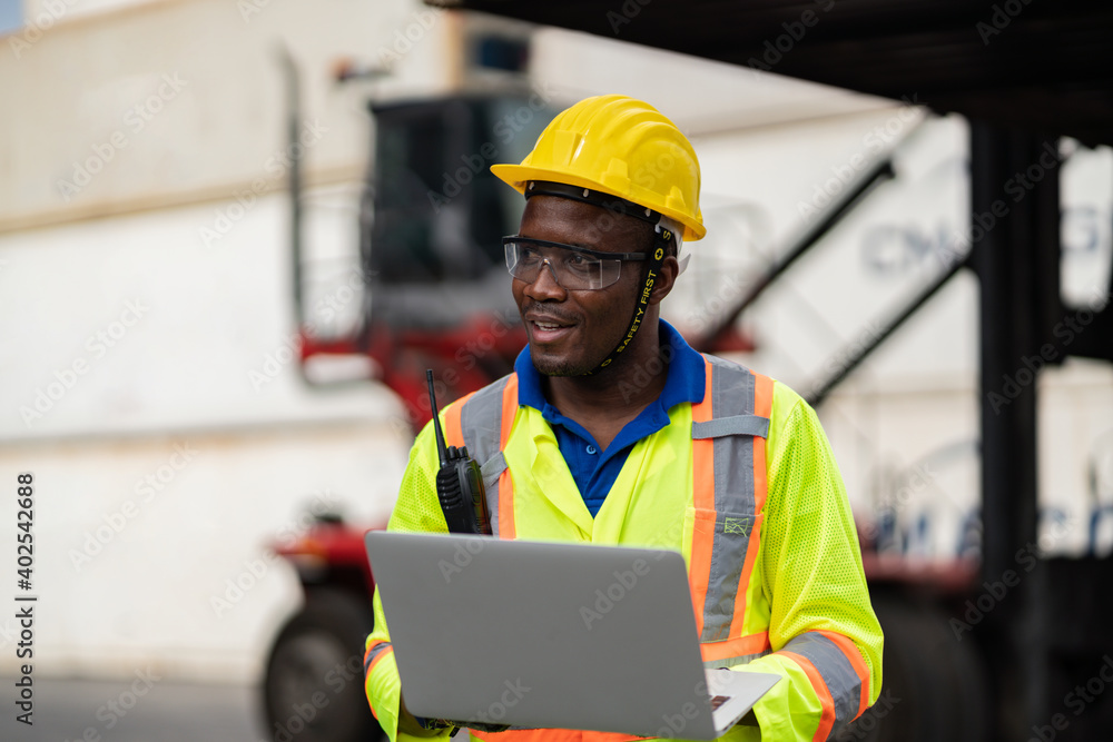 African technician dock worker in protective safety jumpsuit uniform and with hardhat and use digital tablet at cargo container shipping warehouse. transportation import,export logistic industrial African technician dock worker in protective safety jumpsuit uniform and with hardhat and use digital tablet at cargo container shipping warehouse. transportation import,export logistic industrial