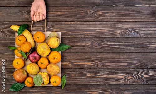 Various ripe  raw fruits in package. Woman s hand holds package  dark restored wooden background. Top view. Food paper bag idea of zero waste. Food delivery  purchase or donation concept. Copy space