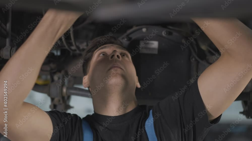 Close-up of concentrated handsome auto mechanic screwing bolts with adjustable wrench. Confident professional Caucasian service man using tool under car in repair shop. Occupation concept. Close-up of concentrated handsome auto mechanic screwing bolts with adjustable wrench. Confident professional Caucasian service man using tool under car in repair shop. Occupation concept.
