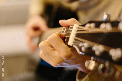 Playing acoustic guitar. The guy is playing chords on the guitar. Black guitar, fingers. Evening light in the house. Metal strings.
