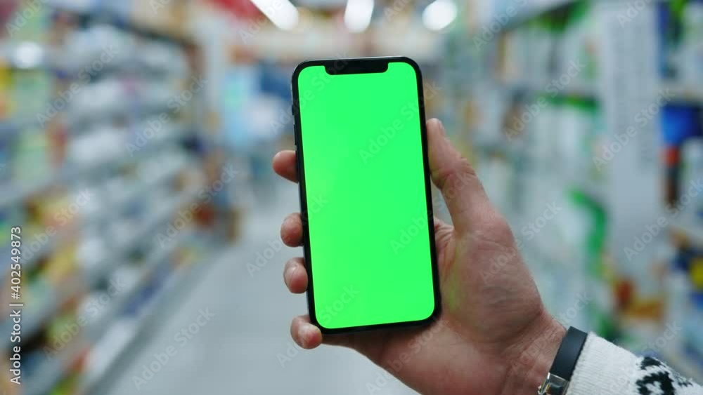 Close up hand use mobile smartphone with vertical green screen in supermarket blurred background. Mockup tapping display chromakey telephone. Slow motion Close up hand use mobile smartphone with vertical green screen in supermarket blurred background. Mockup tapping display chromakey telephone. Slow motion