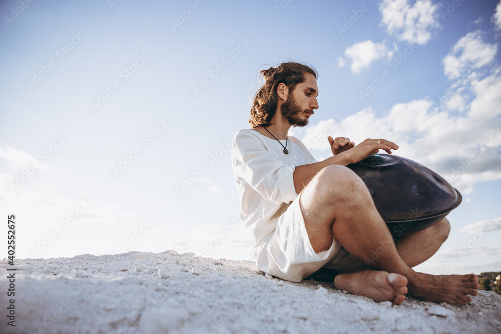 stylish portrait of a young bearded hipster with a modern handpan musical instrument on a city background