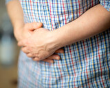 Man with stomach ache. Man in a shirt, holding hands on his stomach, closeup on the hands