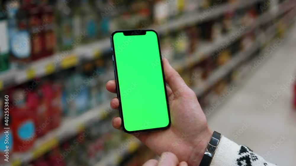Young hands man use mobile smartphone with vertical green screen in supermarket blurred background. Indoors online touchscreen customer blank cellular. Slow motion Young hands man use mobile smartphone with vertical green screen in supermarket blurred background. Indoors online touchscreen customer blank cellular. Slow motion