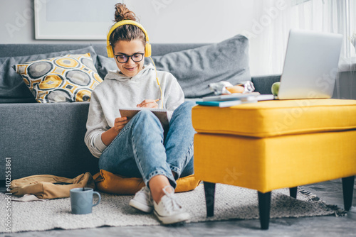 Bild auf Leinwand Student woman learning with headphones and laptop and taking notes at home