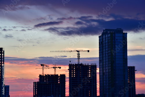 Silhouettes of tower cranes on awesome sunset background. Preparing to pour a bucket of concrete into formwork. Construction a multi-storey residential building. Small sharpness  possible granularity