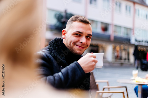 Young man sits outside in a street cafe at the market place and drinks a coffee