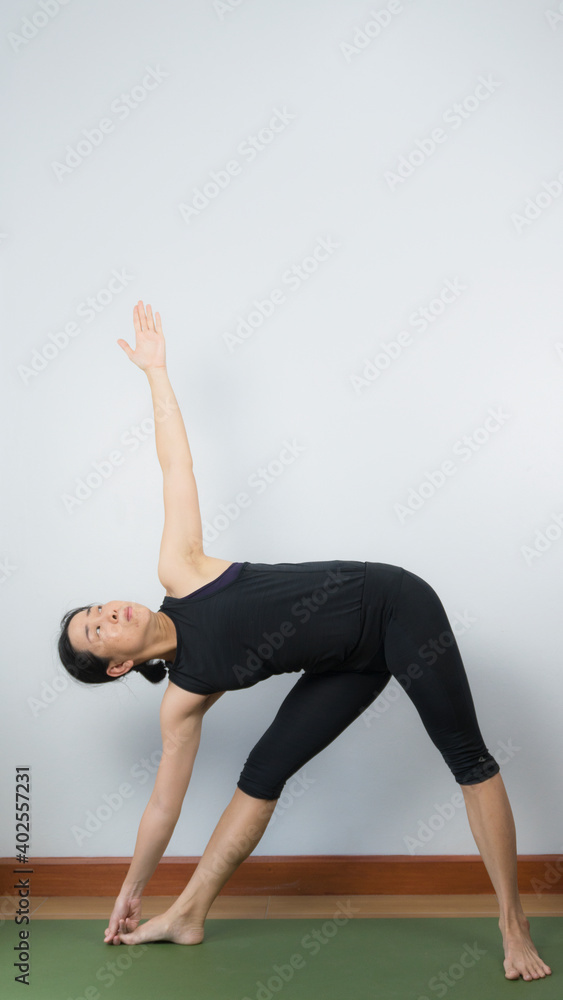 Asian young woman wear a black yoga outfit . Practicing yoga Standing Asanas Action UTTHITA TRIKONASANA (Extended triangle pose).Home yoga practice on white background