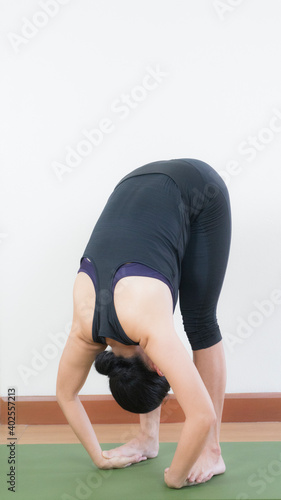 Asian young woman wear a black yoga outfit . Practicing yoga Standing Asanas Action PADAHASTASANA (Hand to foot pose) .Home yoga practice on white background photo