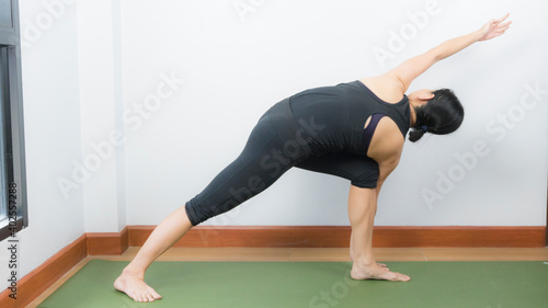Asian young woman wear a black yoga outfit . Practicing yoga Standing Asanas Action PARIVRITTA PARSVAKONASANA (Revolved side angle pose).Home yoga practice on white background
