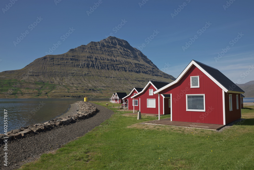 Traditional red painted wooden panel house with mighty Holmatindur mountain in the background in Eskifjordur, East Iceland