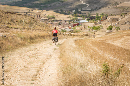 a pilgrim women cycling a dirt road entering Hontanas village, province of Burgos, Castile and Leon, Spain
