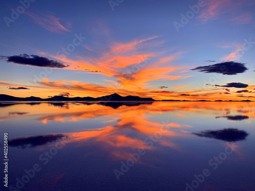 Spectacular sunset  over lake surreal landscape dramatic sky, orange cloudscape over blue sea water, fiery heaven, mediation, zen, tranquility, amazing nightfall nature. © OLENA