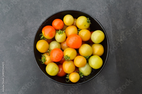 Top view of fresh cherry tomatoes or the scientific name called as Solanum lycopersicum in the black bowl over black background.