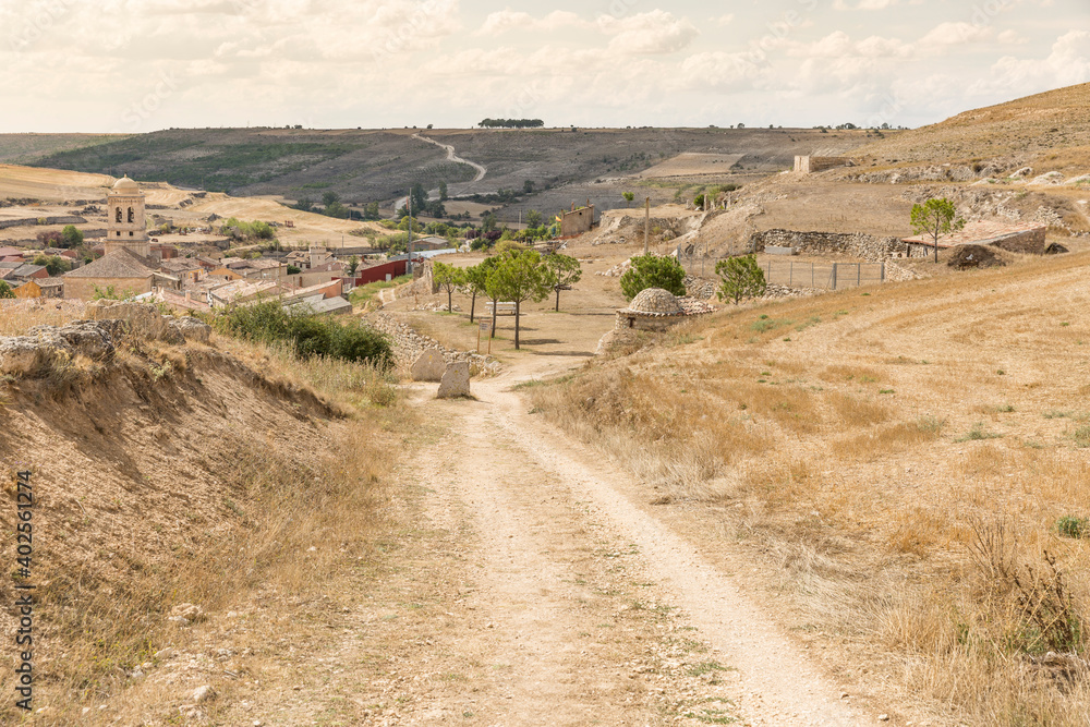 Landscape in summer with a dirt road entering Hontanas village, province of Burgos, Castile and Leon, Spain