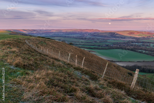 The full moon setting over the Lewes Downs in the north west.  From Firle Beacon on the South Downs Way East Sussex south east England