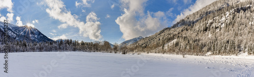 Verschneite Berge am gefrorenen See im Chiemgau bei blauen Himmel mit Wolken