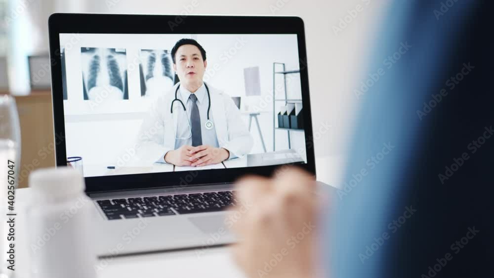 Young Asia lady using computer laptop talk about a disease in video conference call with senior doctor online consultation in living room at home. Social distancing, quarantine for coronavirus concept Young Asia lady using computer laptop talk about a disease in video conference call with senior doctor online consultation in living room at home. Social distancing, quarantine for coronavirus concept