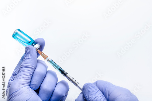 Hands in blue gloves draw medicine from a vial with a syringe on a white background