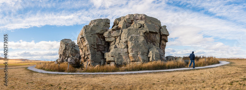 Big Rock Erratic Okotoks tourist destination giant boulder in the prairies landscape at sunset golden hour. Person walking on pathway at point of interest panorama