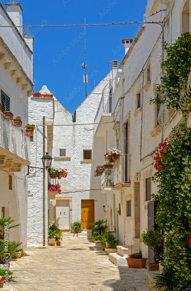 Sunny small street with white buildings and flower decoration in the city of Locorotondo, Italy