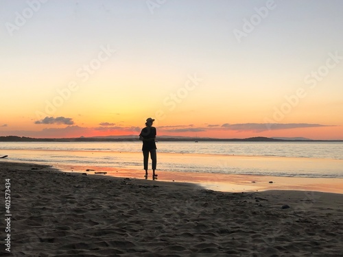 A photographer walks along the beach at Noosa Heads capturing sunset photos