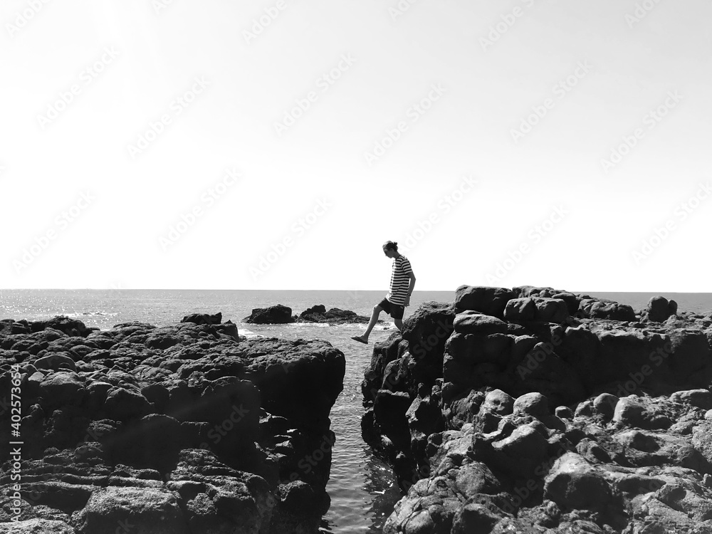 Black and white - stepping across a crack in the rocks with the ocean below