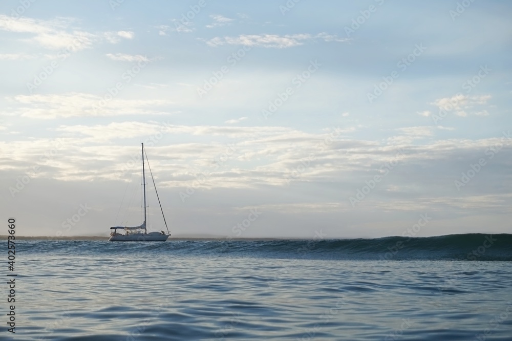 A sailing boat drifts behind an oncoming wave in brilliant light A sailing boat drifts behind an oncoming wave in brilliant light