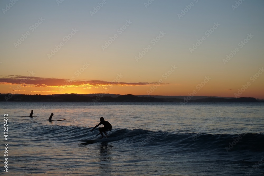 A longboard surfer riding a small wave at sunset crouches down low - Gold Coast
