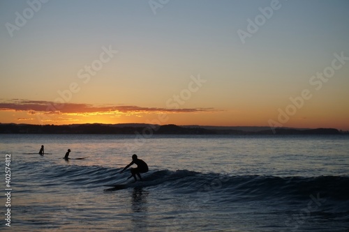 A longboard surfer riding a small wave at sunset crouches down low - Gold Coast