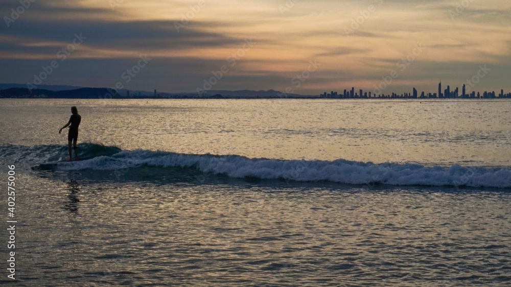 A surfer crusing on a small wave at sunset, Surfers Paradise on the horizon - Australia