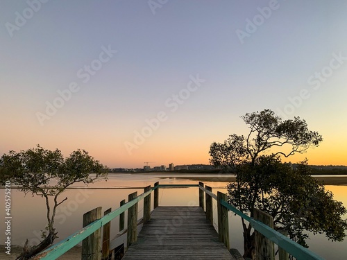 The sun setting at the end of a colourful jetty. The skyline of the sunshine coast in the distance - Australia © William