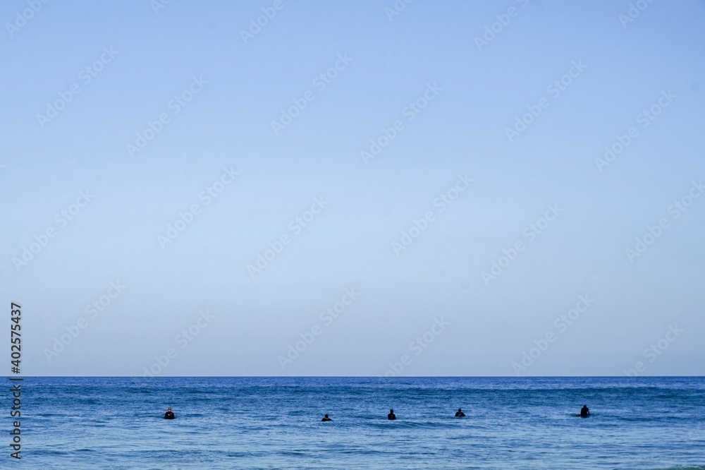 A minimalistic surf line up. Blue skies and blue waters with a small group of surfers sat on thier boards, Cornwall