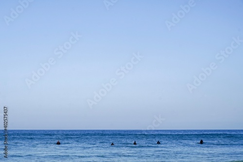 A minimalistic surf line up. Blue skies and blue waters with a small group of surfers sat on thier boards, Cornwall