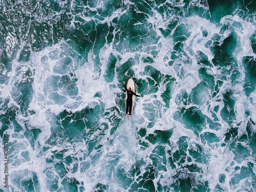 Canvas Print Aerial view of a surfer on a wooden surfboard paddling through rough blue ocean