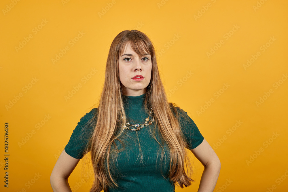 Closeup portrait looking straight at the camera, waist up of cheerful. Young attractive woman, dressed green shirt blonde hair, yellow background Closeup portrait looking straight at the camera, waist up of cheerful. Young attractive woman, dressed green shirt blonde hair, yellow background