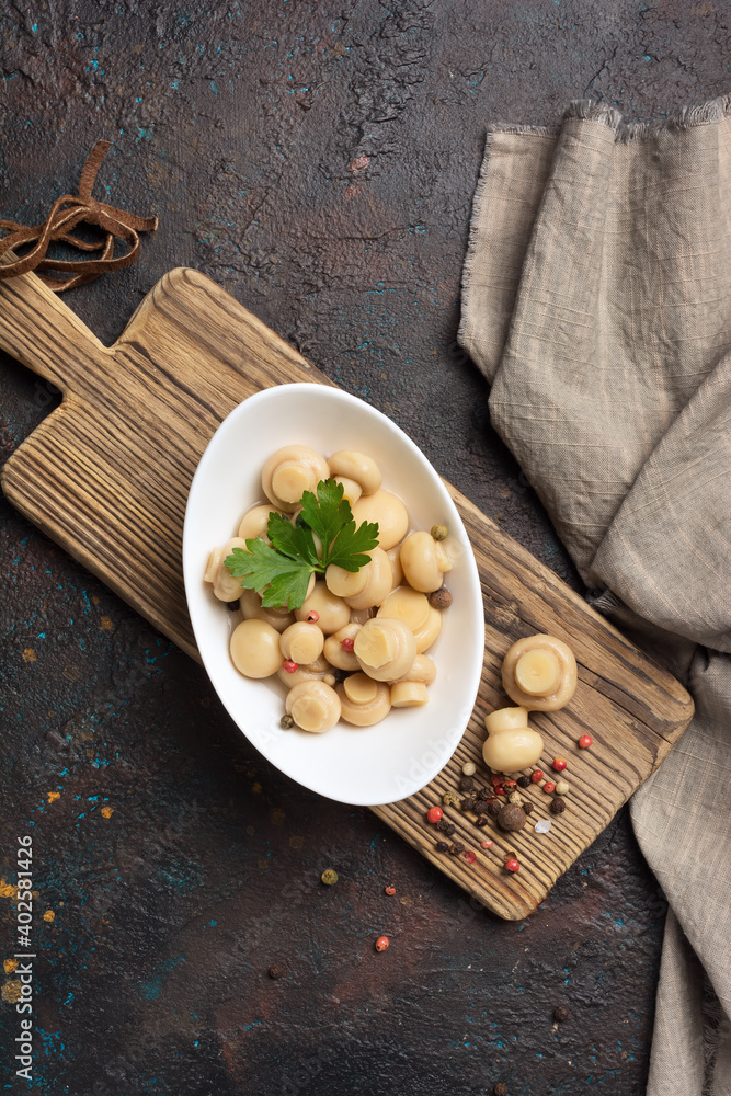 Fototapeta premium Marinated champignon mushrooms with spice in white bowl on wooden board