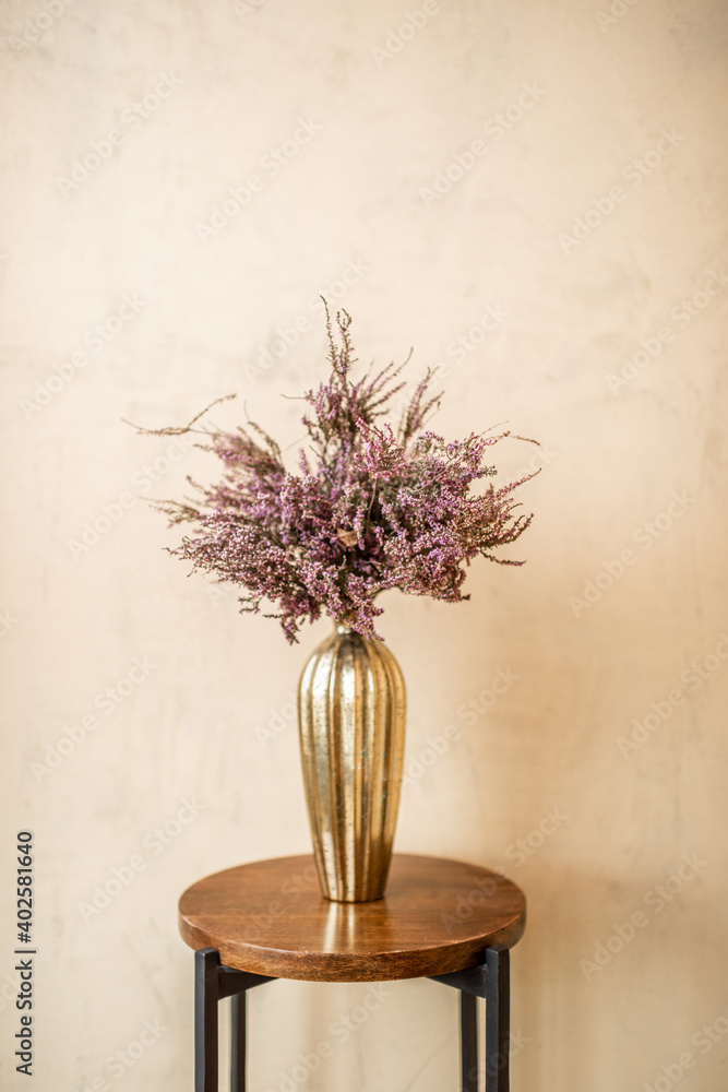 Fototapeta premium Dried Calluna flower in a gold vase on a beige wall background
