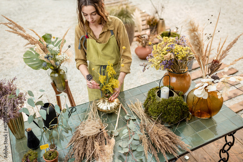 Fotografia Young woman making compositions of dried and fresh flowers and herbs at the workshop outdoors