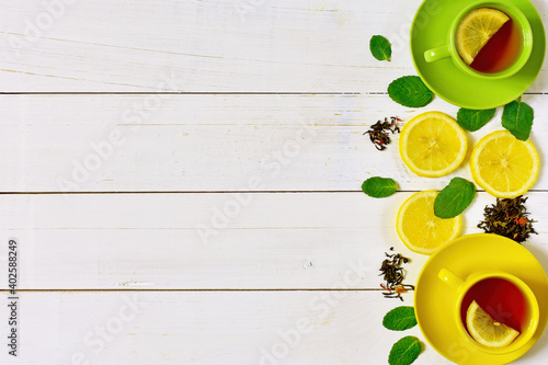 Background of multicolored cups of tea, lemon and mint on a white wooden background.
