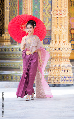 THAILAND ,Beautiful woman in a pink Thai dress or a traditional Thai dress is spreading a red umbrella in a Thai temple.