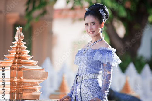 Beautiful Thai woman wearing a Thai Chitralada dress holds a garland in her hand in a Buddhist temple in Thailand which is architecturally beautiful. photo