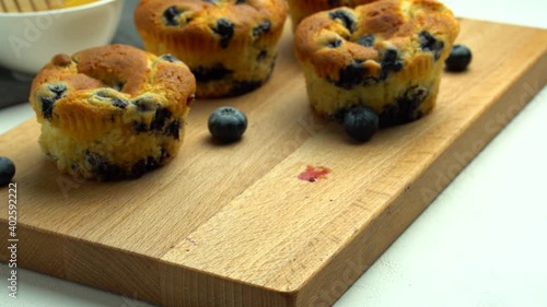 Blueberry muffins on a wooden board on a white background. The chef tries a piece of muffin. Close-up of the texture of a cupcake with berries
