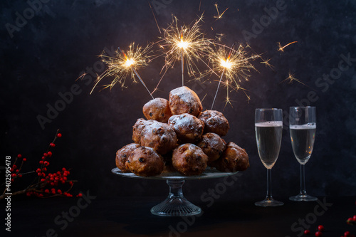 Horizontal shot of a stack of oliebollen (translation: Dutch dough firitters) with sparklers and two glasses of champagne on black background