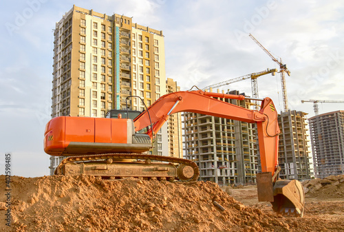 Excavator during excavation aond road construction works at construction site on sunset background. Backhoe on foundation work in sand pit.Tower crane on constructing new building photo