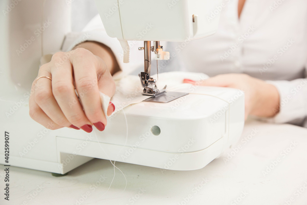 Girl sews cotton white fabric on the sewing machine. Close-up.

