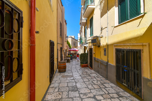 Fototapeta Naklejka Na Ścianę i Meble -  A woman walks down a colorful narrow alley towards a cafe in the Italian city of Brindisi Italy, in the Puglia region.