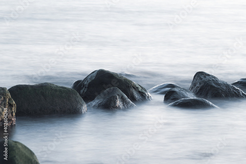 Long exposure of sea and rocks. Boulders sticking out from smooth wavy sea. Tranquil scene.