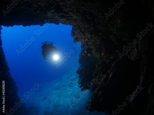 Scuba divers underwater exploring lightcaves blue ocean scenery with torch 