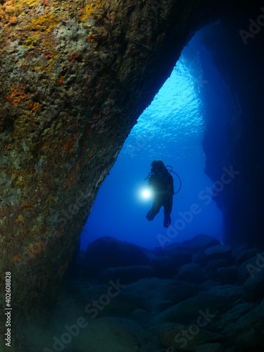 Scuba divers underwater exploring lightcaves blue ocean scenery with torch 